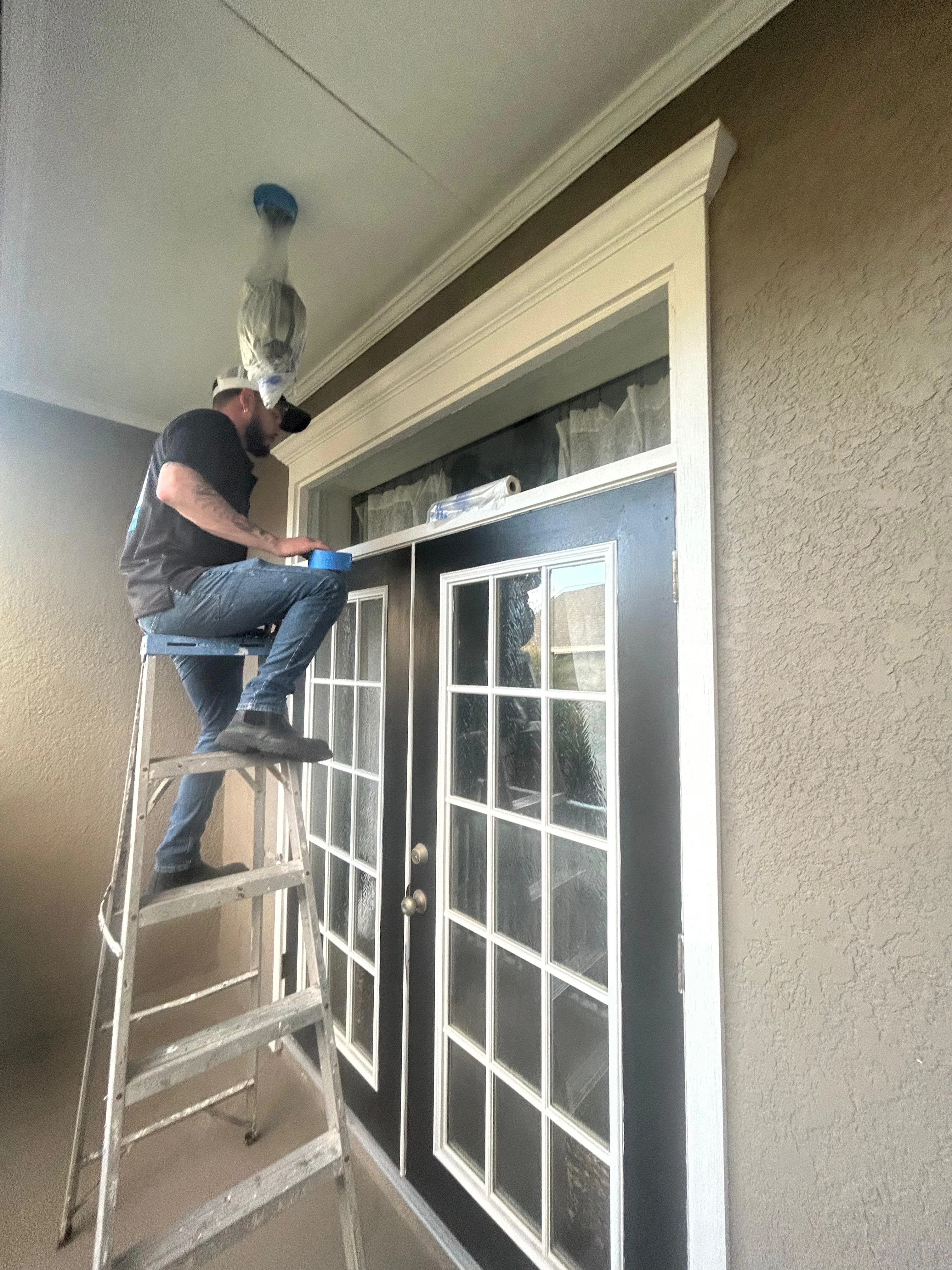 Contractor installing and painting front door trim on ladder — Central Florida Renovations